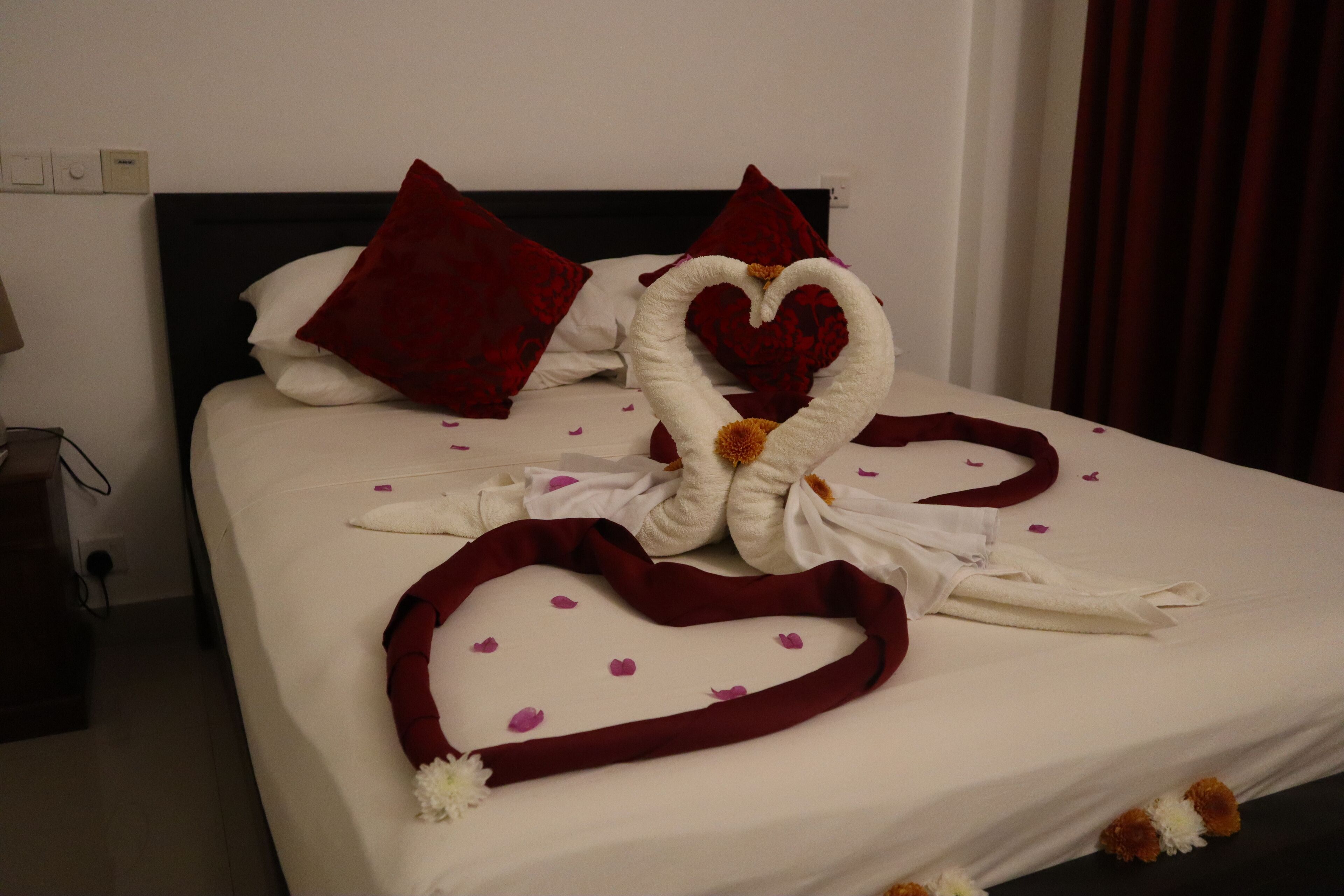 Una cama bien hecha con una toalla dispuesta en forma de corazón y almohadas rojas.