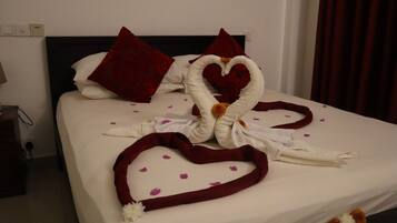 Una cama bien hecha con una toalla dispuesta en forma de corazón y almohadas rojas.