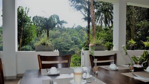 Mesa para dos servida con vistas a un bosque frondoso a través de grandes ventanales.