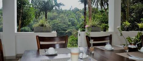 A dining table set for two with a view of a lush forest through large windows.