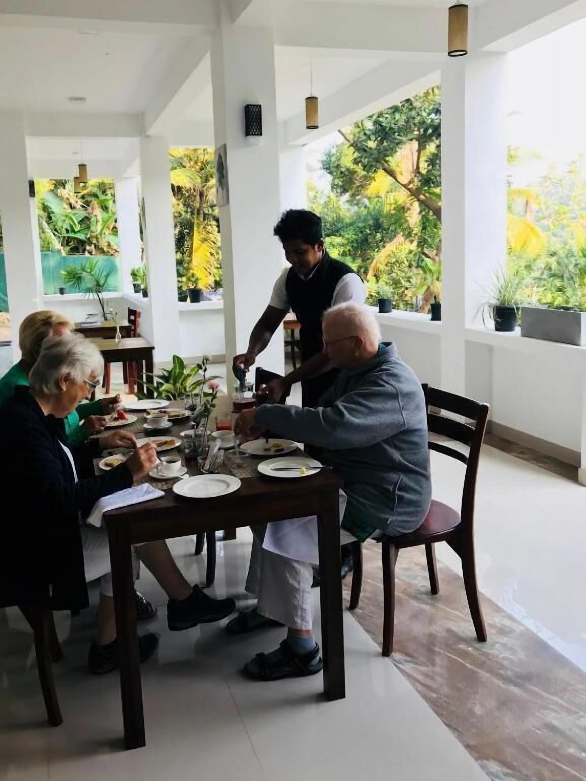 Un coin repas avec une table dressée pour quatre personnes, entouré de grandes fenêtres d’où l’on peut voir des plantes à l’extérieur.