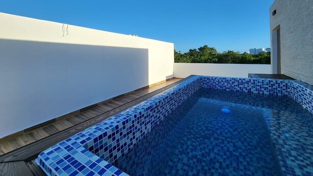 Una piscina sul tetto con piastrelle di mosaico blu, circondata da un solarium in legno e pareti bianche.
