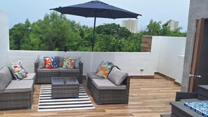 Una terrazza sul tetto con mobili in vimini, un tappeto a righe e un ombrellone grande.