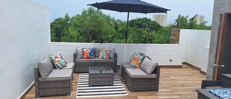 Una terraza en la azotea con muebles de mimbre, un tapete a rayas y un paraguas grande.
