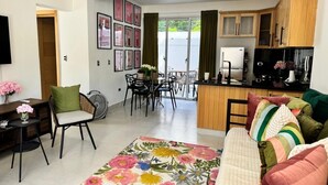 Un soggiorno moderno con un divano, una zona pranzo con sedie, una cucina con mobili in legno e una porta scorrevole in vetro che dà su un balcone.