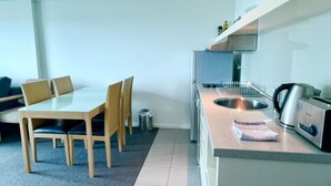 A compact kitchen with a dining table, chairs, a kettle, a toaster, and a sink. - Pandanas Apt 8 (18th fl, Sunrise & Harbour Views) (Darwin City)