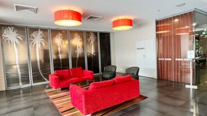A modern lobby with a red sofa set, a glass partition with palm tree designs, and a wooden door. - Pandanas Apt 8 (18th fl, Sunrise & Harbour Views) (Darwin City)
