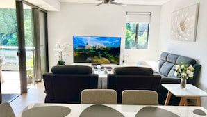 A modern living room with a flat-screen TV, a ceiling fan, a dining area with a white table, and a sofa.