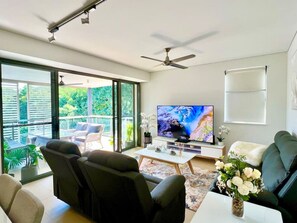 A modern living room with a flat-screen TV, comfortable seating, a ceiling fan, and a balcony with outdoor furniture. - Waterfront Escape (2 bedrooms) (Darwin City)