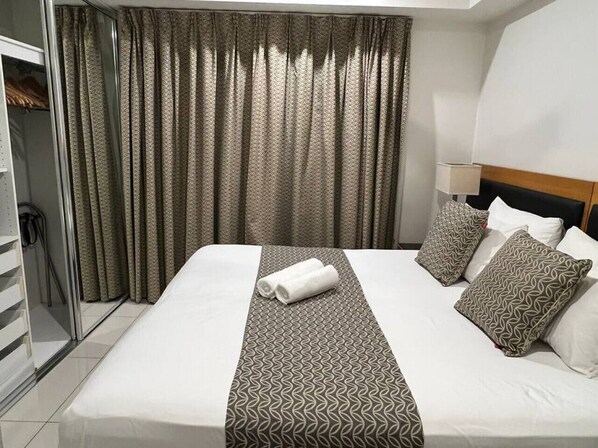 A neatly made bed with patterned pillows, a rolled towel, and a patterned bed runner. - Sky high with harbour views (Darwin City)