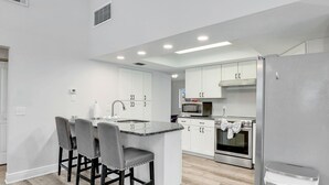 A modern kitchen with white cabinets, a granite countertop, a stainless steel refrigerator, and a built-in oven.