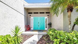 A building with a turquoise door, red chairs, and a palm tree.