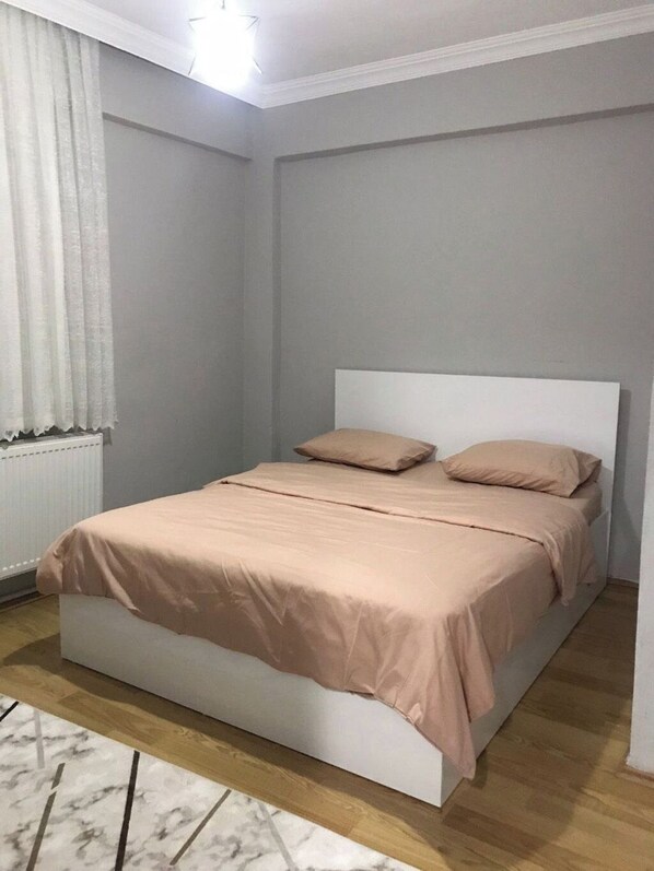 A bedroom with a bed, a radiator, and a window with curtains. - Rova Suit (Tokat)