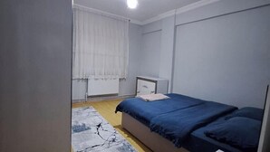 Een slaapkamer met een bed, nachtkastje, gordijnen en een plafondlamp.