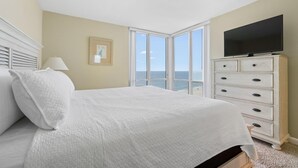 Un dormitorio con una cama grande, un aparador, un televisor y una ventana con vista al océano.