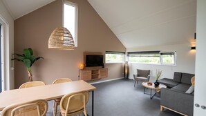A modern living room with a dining area, a sofa, a TV, and a large window. - Villa in Breskens Near the Beach (Breskens)