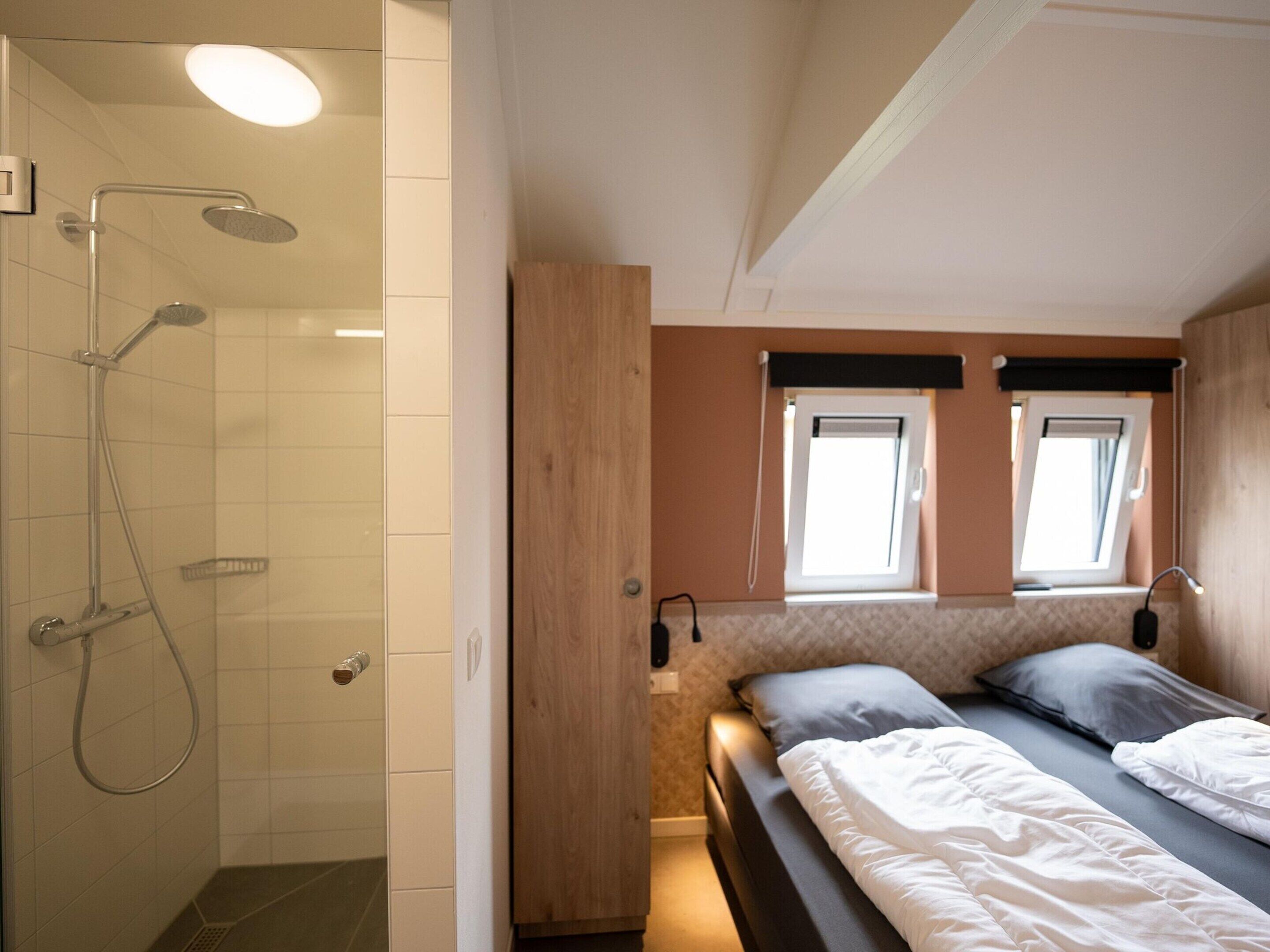 Ein gemütliches Schlafzimmer mit Dusche, zwei Fenstern und einem Bett mit Kissen.