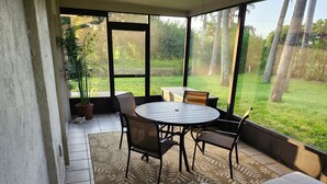 Un patio cubierto con una mesa redonda y sillas, una planta en maceta y vistas a un área verde.