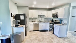 Una cocina moderna con armarios blancos, electrodomésticos de acero inoxidable y piso de baldosas.