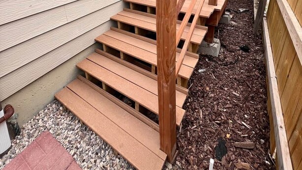 Um deck de madeira com escadas que levam a uma casa com revestimento e um aparelho de ar condicionado.