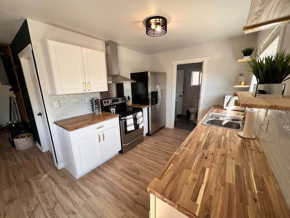 A kitchen with white cabinets, a wooden countertop, stainless steel appliances, and a wooden floor.