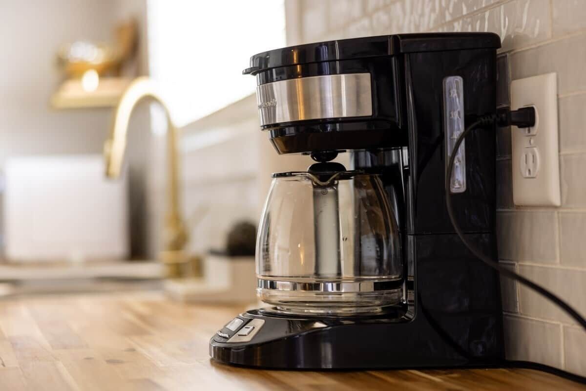 A coffee maker on a kitchen counter with a tiled backsplash and a gold faucet.