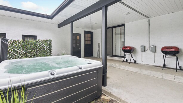 A modern outdoor patio with a hot tub, two barbecue grills, and a white brick wall.