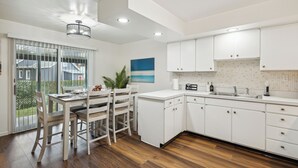 A modern kitchen with white cabinets, a wooden dining table, and a large window with a view of the outside.