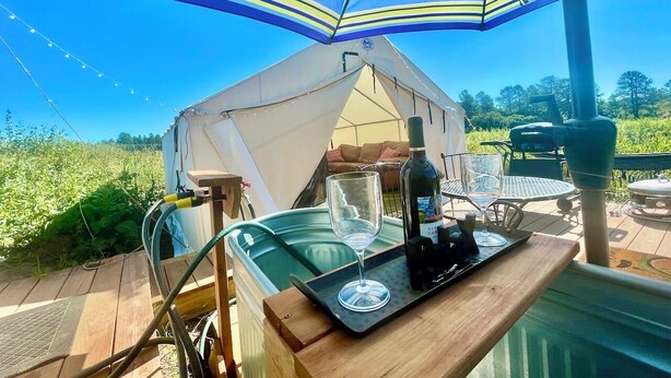 A tented outdoor area with a hot tub, a bottle of wine, and a table with a glass. - “Queen's Quarters” Cozy Outdoor Glamping • Hot Tub (Monument)