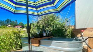 A metal table with a metal grill, a metal container with a wooden shelf, and a blue and yellow striped umbrella. - “Queen's Quarters” Cozy Outdoor Glamping • Hot Tub (Monument)