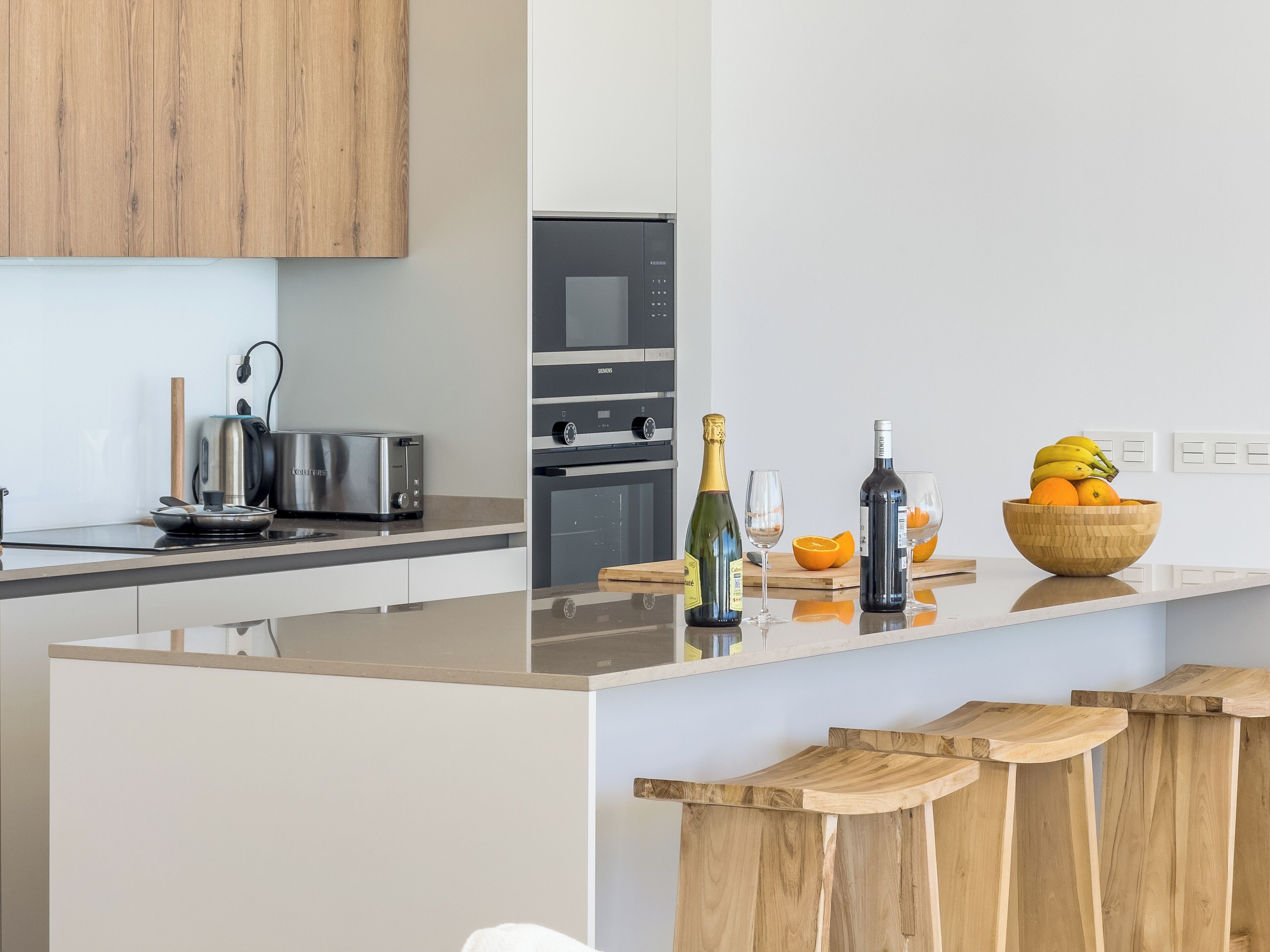 Une cuisine moderne dotée d’un îlot central, d’appareils électroménagers en acier inoxydable et de tabourets de bar en bois.