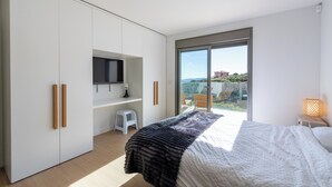 Una camera da letto con un letto, una televisione a muro, uno sgabello e una finestra con vista sull'esterno.