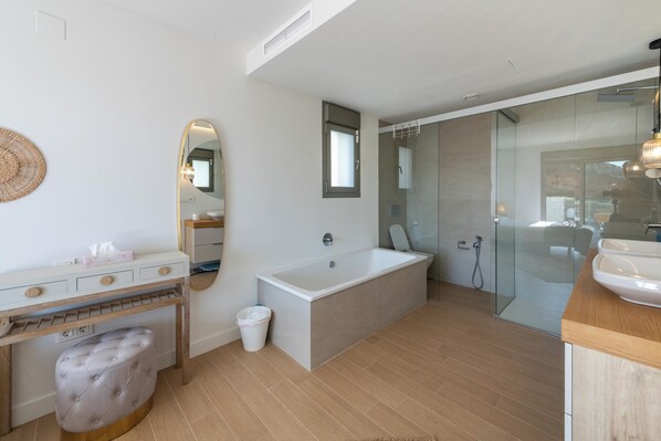Un baño moderno con una bañera grande, cabina de ducha con vidrio, tocador con espejo y un taburete.
