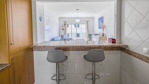 Una cocina con encimera de granito, dos taburetes de bar y vistas al salón a través de una puerta abierta.
