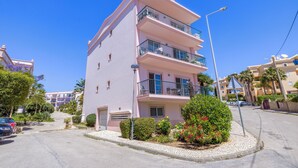 Un edificio residencial rosa de varios pisos con balcones, una entrada para coches y zonas verdes circundantes.