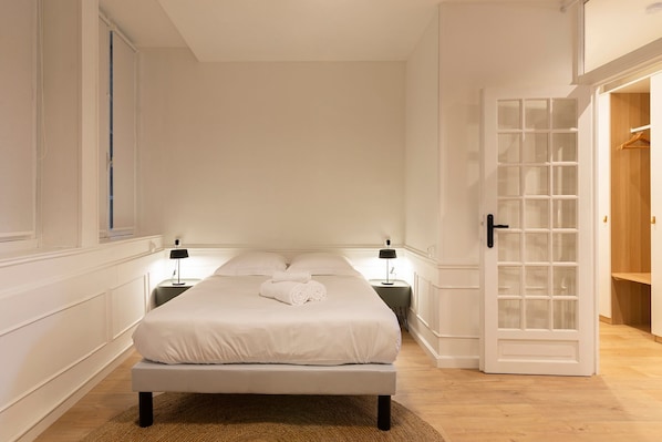 Een slaapkamer met een bed, twee nachtkastjes, een kledingkast en een deur met ruitpanelen.