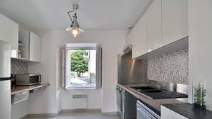 A modern kitchen with white cabinets, stainless steel appliances, and a view through the window. - Duplex Plancoët - Pour 4p, à 15 min de la plage (Créhen)
