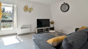 A modern living room with a grey sofa, a flat-screen TV, a small round table, and decorative wall art. - Duplex Plancoët - Pour 4p, à 15 min de la plage (Créhen)
