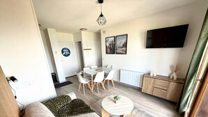 A modern living room with a sofa, coffee table, dining area with chairs, a TV, and a cabinet. - Le Nid des 3 Sommets - Proche station de ski (Villarembert)