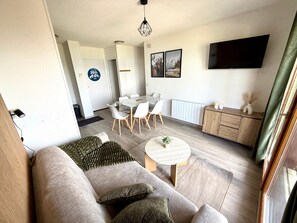 Un salon moderne comprenant un canapé, une table basse, un coin repas avec des chaises, un téléviseur et un meuble.