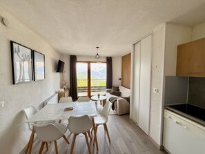 A modern kitchen with a built-in stove, a dining area with a table and chairs, a sofa, and a view of mountains through the sliding glass door.