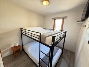 Une chambre avec un lit superposé, un petit tabouret en bois, une fenêtre avec vue et un luminaire au plafond.