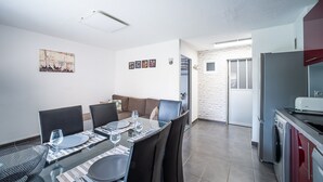 A modern dining area with a glass table, chairs, and a sofa. There is a kitchen area with a refrigerator and a washing machine. - Le Cosy Canétois - A 20 min de la plage (Canet-en-Roussillon)