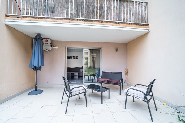 A balcony with a table and chairs, a covered umbrella, and a sliding glass door leading to an interior space.