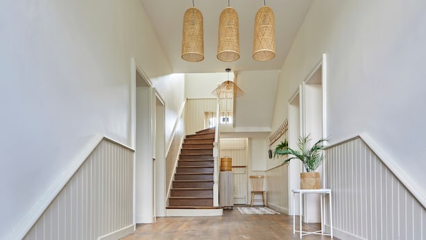 A wooden staircase with white wainscoting, a hanging wicker light fixture, and a potted plant on a small table. - Le Logis du Clergé - Grande maison pour 15p (Lassy)
