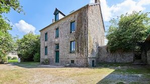 A stone building with a green door and windows, surrounded by trees and a grassy area. - Le Logis du Clergé - Grande maison pour 15p (Lassy)