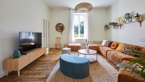 A modern living room with a TV, sofa, ottoman, and coffee table. - Le Logis du Clergé - Grande maison pour 15p (Lassy)