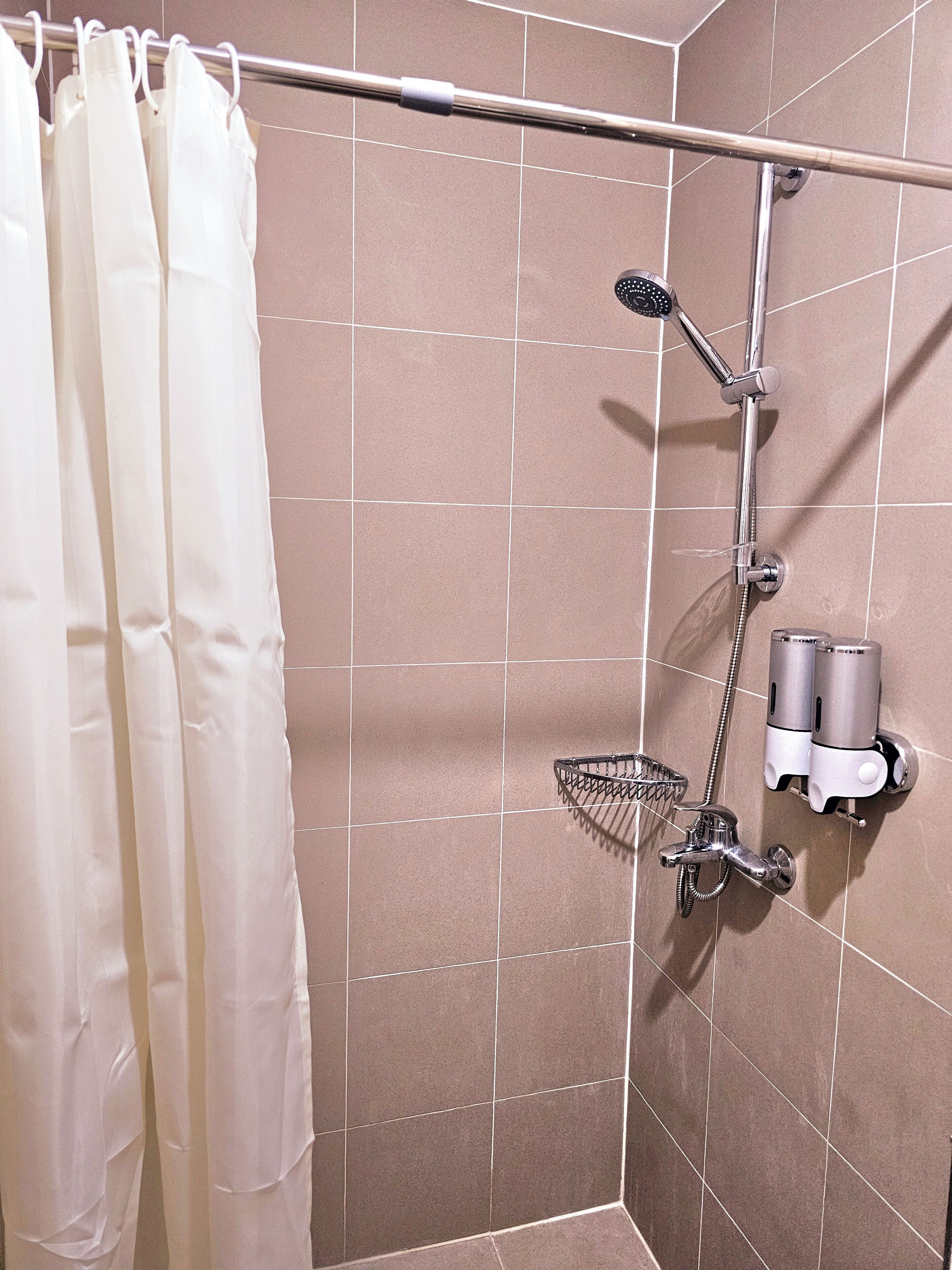 Un espacio de ducha con cortina, un cabezal de ducha de mano, un grifo empotrado y un dispensador de jabón.