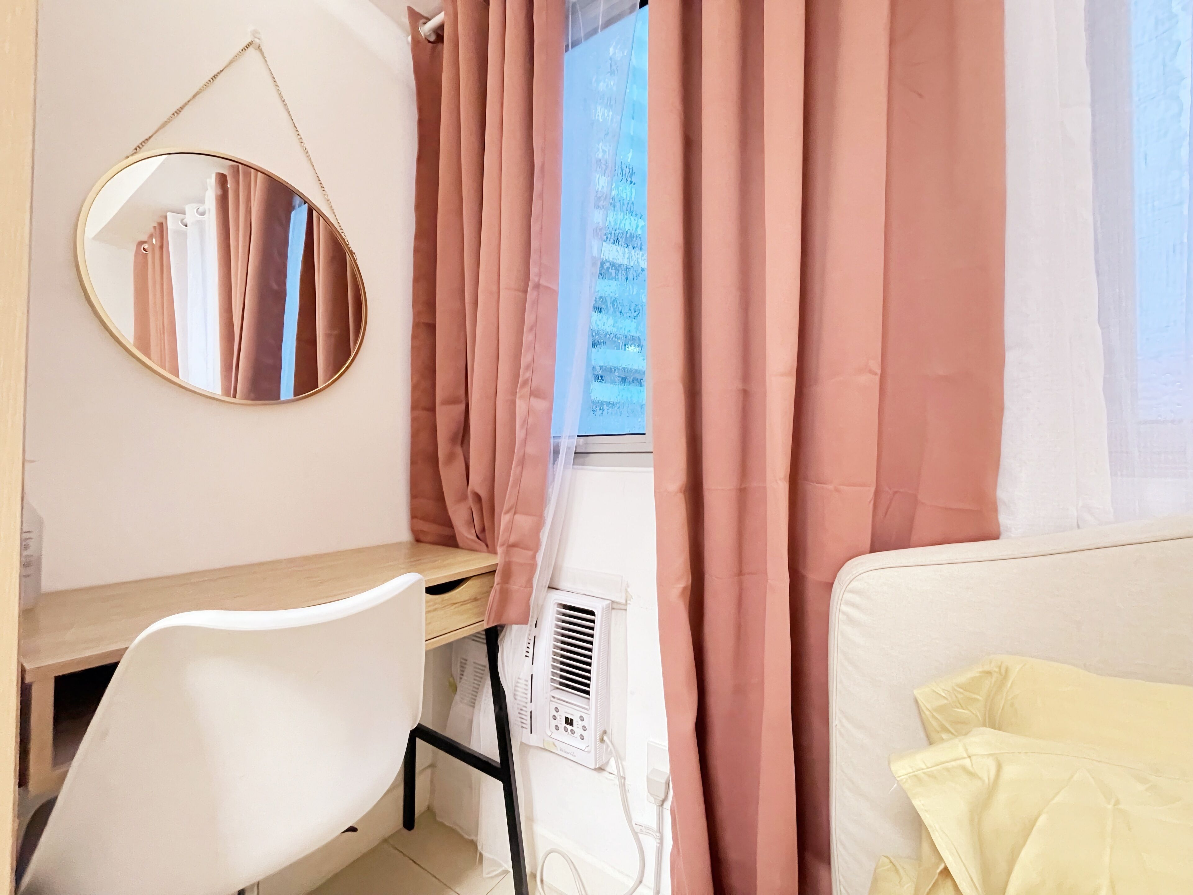 A room with a desk, a chair, a bed, and a window with pink curtains.