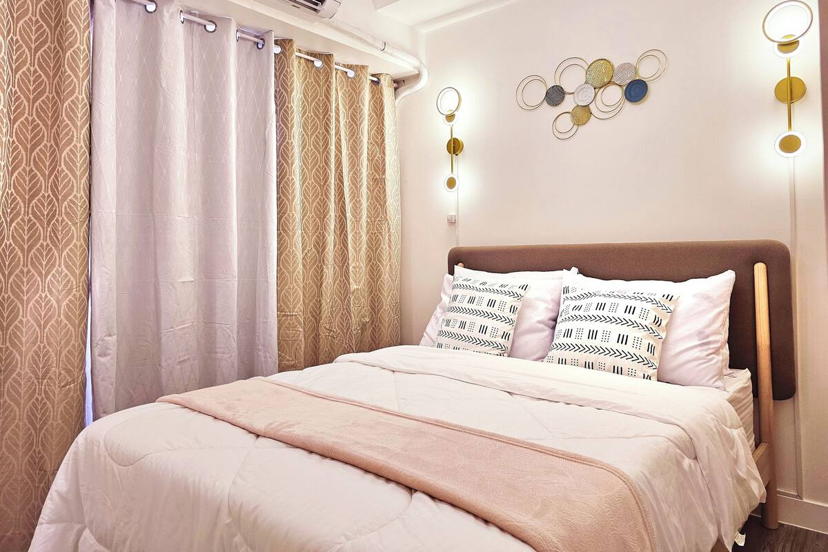 A neatly arranged bedroom with a bed, curtains, wall decor, and an air conditioning unit.
